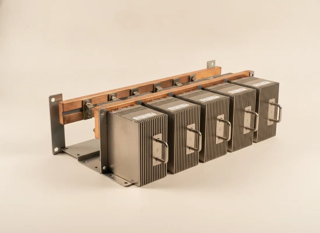 A DC power shelf with six hot-swap rectifier modules and heavy tinned copper busbars with blind-mate clips behind them.