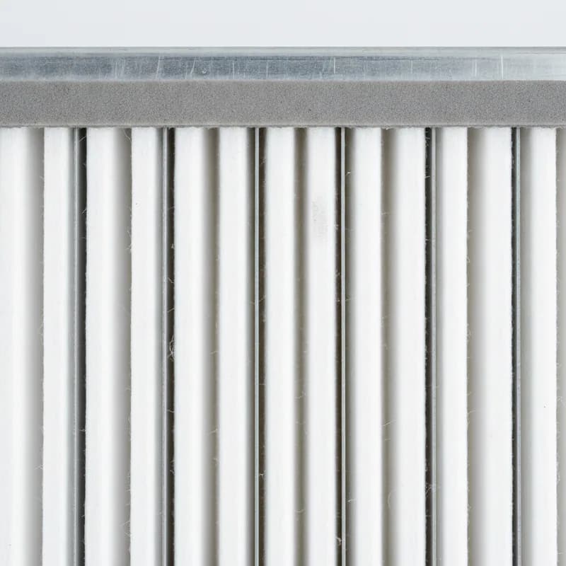 A macro view across the pleats of a synthetic panel air filter, with aluminium spacer combs between the media and a foam-gasketed galvanised frame edge in one corner.
