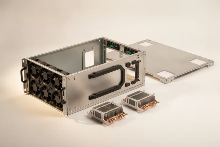 An empty 4U server chassis with its cover lifted off, showing a full-width wall of fan modules, empty power-supply bays and air baffles, with two finned copper-heat-pipe heatsinks on the bench beside it.